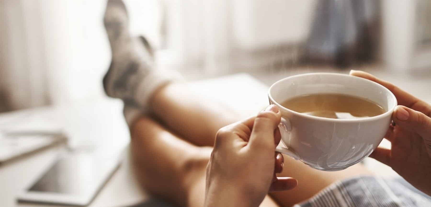 persona rilassata con i piedi poggiati sul tavolino e una tazza di thé fumante in mano