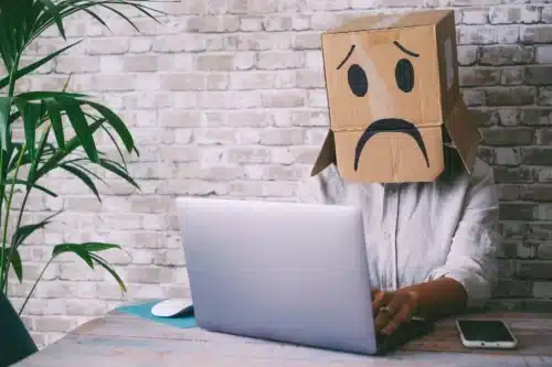 dipendente vittima di mobbing al lavoro con una busta di carta sul volto a rappresentare espressione triste