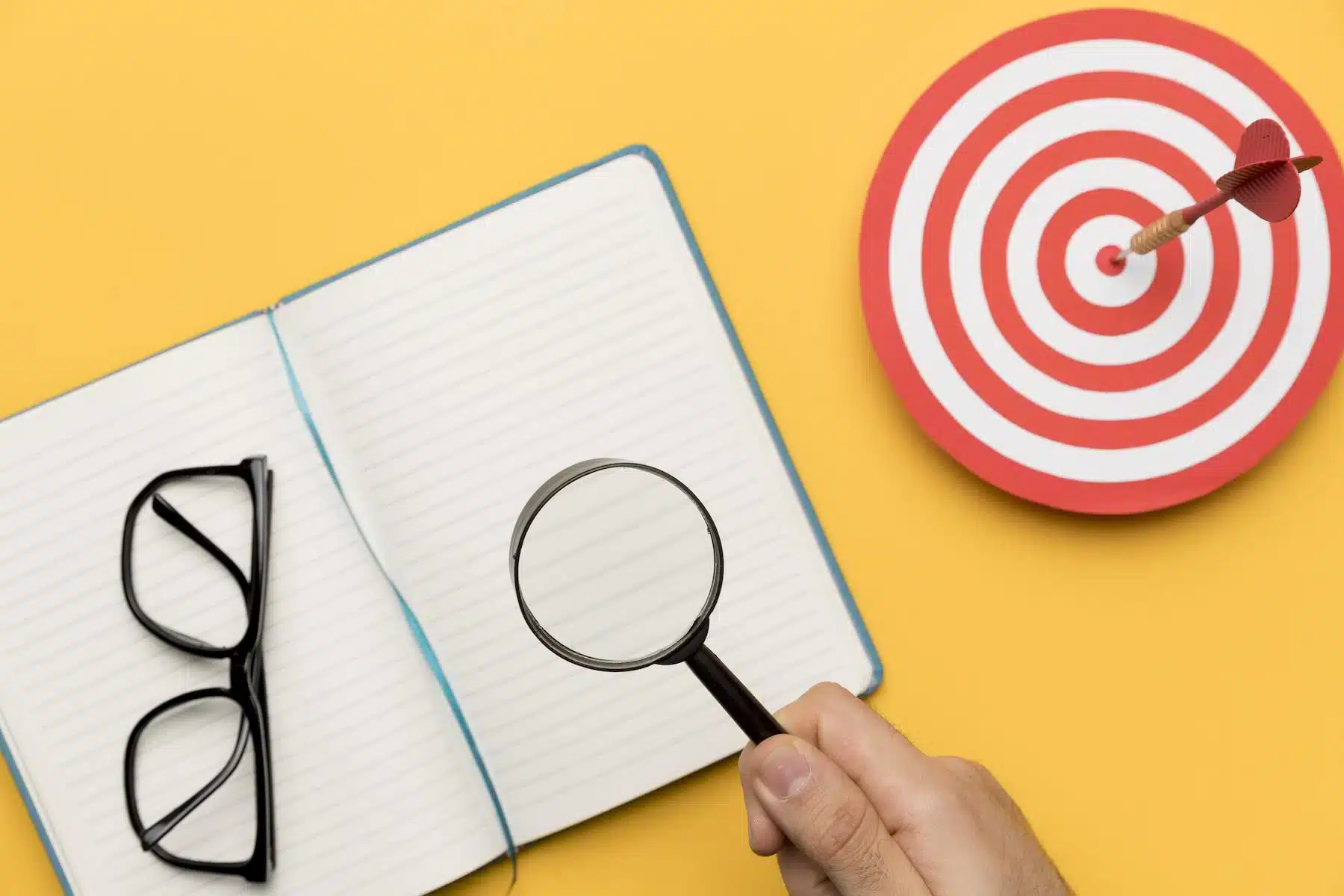 MBO: cos’è il Management by Objectives e come funziona la Gestione per Obiettivi mbo gestione per obiettivi: lente di ingrandimento sull'agenda e immagine di bersaglio rosso con freccia al centro
