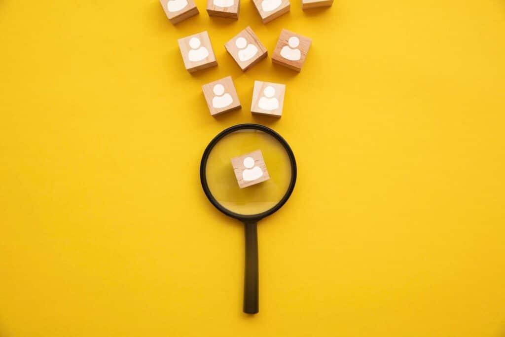 talent acquisition: lente di ingrandimento su sfondo giallo che analizza blocchi di legno con sagoma di persone