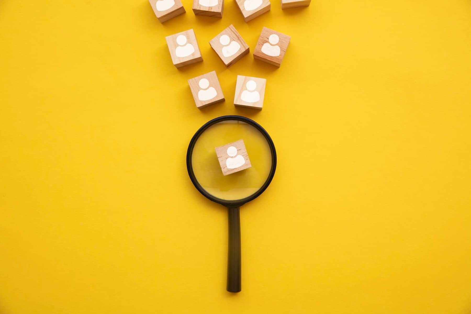 Cos’è e come costruire una strategia efficace di Talent Acquisition talent acquisition: lente di ingrandimento su sfondo giallo che analizza blocchi di legno con sagoma di persone